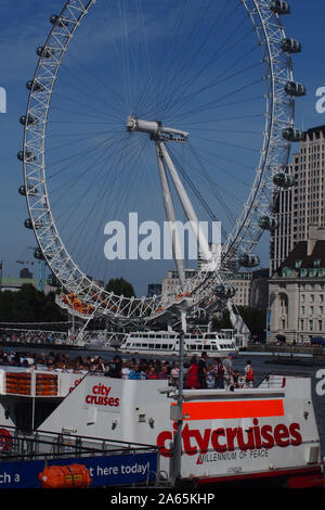 A view of the London Eye from the opposite side of the River Thames with a citycruises passenger boat in the foreground with many people on board Stock Photo