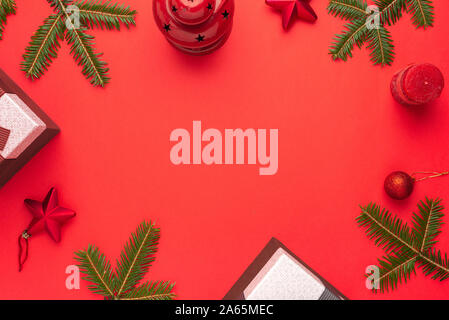 Christmas background composition on red surface. Christmas tree branches, gifts and decorations. Copy space in the middle. Flat lay, top view. Stock Photo