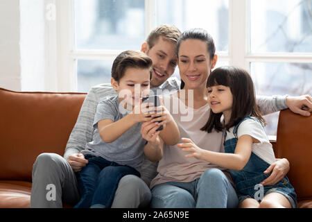Excited family hugging, entertaining, using mobile phone. Stock Photo