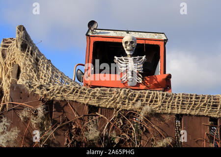 A scary Skeleton sitting on a farm machine to illustrate the concept of Halloween Stock Photo