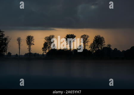 Tree silhouettes in the distance on a rainy summer evening at sunset in the Lithuanian countryside. Reflection on the gray roof of the car Stock Photo