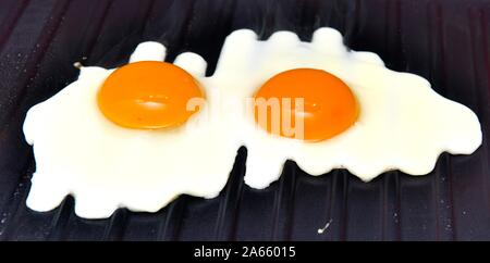 Two eggs frying on a griddle pan Stock Photo