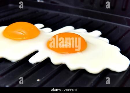 Two eggs frying on a griddle pan Stock Photo