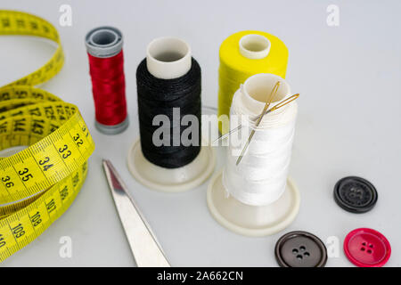 sewing thread bobbins with two needles, three black, red and brown colored buttons, scissors a seamstress or tailor tape measure on white background Stock Photo