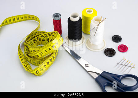 sewing thread bobbins with two needles, three black, red and brown colored buttons, scissors, needle set and a seamstress or tailor tape measure on wh Stock Photo