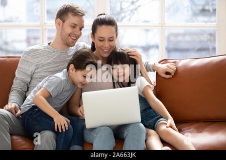 Joyful family sitting on couch, looking at laptop screen. Stock Photo