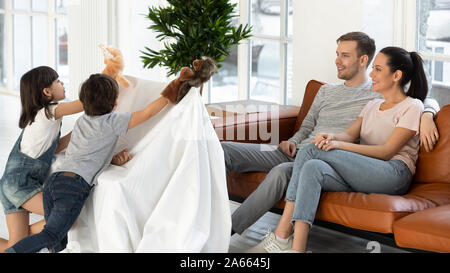 Happy millennial parents sitting on sofa, watching puppet show. Stock Photo