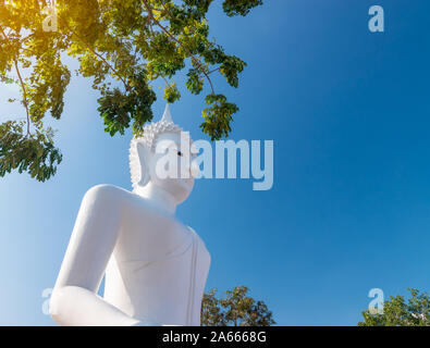 White Buddha statue used as amulets of Buddhism religion. Buddha statue sitting in public temple with blue sky background. Stock Photo