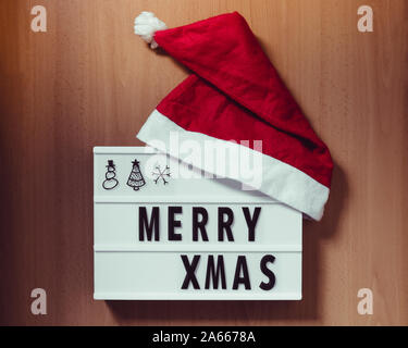 Lightbox with words "Merry Xmas" and red santa hat on wooden background Stock Photo