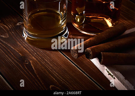 Still life with glass and bottle of alcohol, whiskey or brandy or rum. Three cuban cigars in a wooden box with space for text. Stock Photo