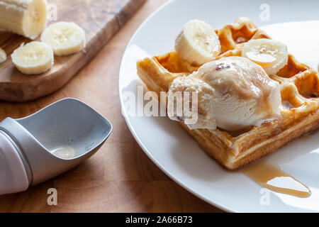 Banana waffle close-up. Delicious breakfast dessert meal prepared on plate. Sweet fried waffle with vanilla praline ice cream and maple syrup in close Stock Photo