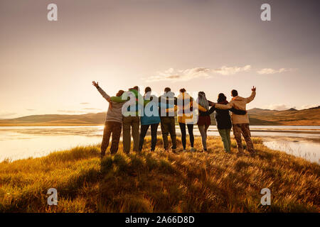 Big happy family is standing and hugging together against lake in mountains and sunset sky Stock Photo