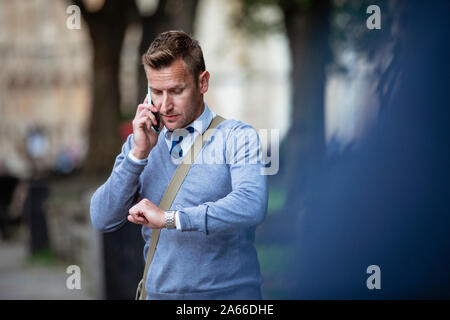 Businessman on his way to work while talking on the phone and checking the time. Stock Photo