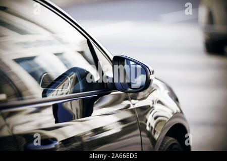 On a beautiful polished car that drives past the building, a rearview mirror reflecting the blue sky. Stock Photo