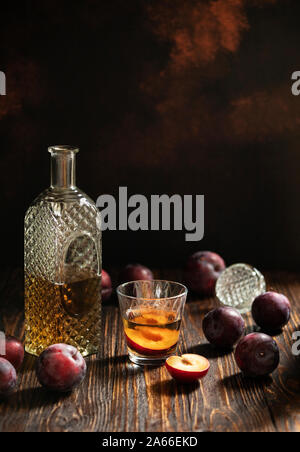 Rakia or rakija traditional Balkan fruit brandy. Plum brandy sljivovica in a glass and decanter on a wooden table and dark background. Vertical Stock Photo