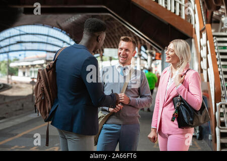 Two businessmen and one businesswoman standing in a train station having a discussion. They are laughing together. Stock Photo