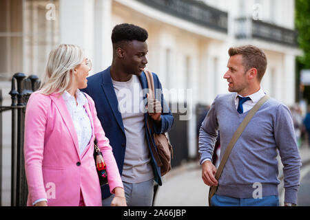 Two businessmen and one businesswoman walking to work while having a discussion. Stock Photo