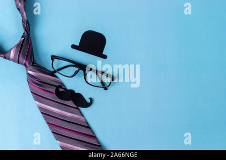 Movember mustache awareness concept. Black sign of hat, mustache, glasses, tie with pale blue background, copy space for text. Stock Photo