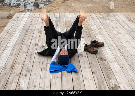 Mature Spanish woman stretching, performing Yoga on beach boardwalk. Stock Photo