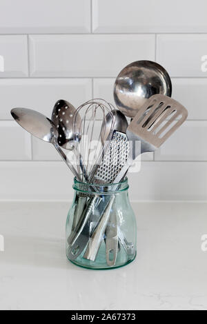 Glass container holding various stainless steel kitchen utensils