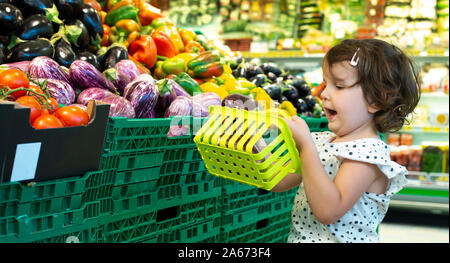 Child shopping eggplants in supermarket. Concept for buying fruits and vegetables in hypermarket. Little girl hold shopping basket. Stock Photo