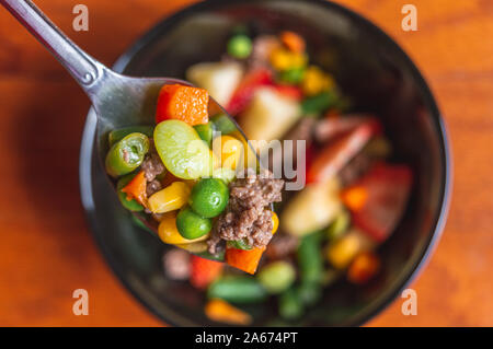Closeup of healthy vegetables salad on a metal spoon over a bowl on a wood table Stock Photo