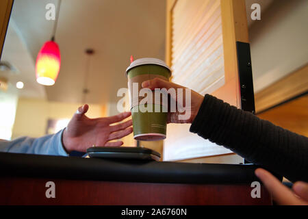 Customer hand passing over a hot beverage to a friend over restaurant partition. Stock Photo