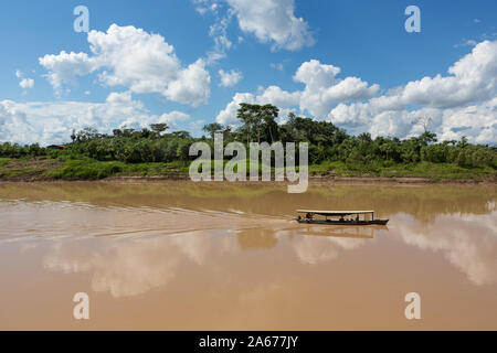 View of rustic wooden motor boat sailing with local people on Purus river in Amazon on sunny summer day with trees on river bank, blue sky and clouds Stock Photo