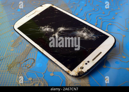Phone with broken screen on the background of printed circuit board. Stock Photo