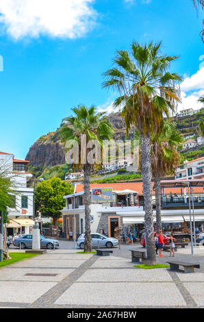 Ribeira Brava, Madeira, Portugal - Sep 9, 2019: Promenade in the Madeiran village photographed from the coast of the Atlantic ocean. Tourists on the streets. Outdoor restaurants and shops. Palm tree. Stock Photo