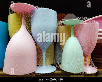 Disposable colored plastic wine glasses close-up. Yellow, blue, pink and green plastic wine glasses are on sale. Disposable plastic tableware for the Stock Photo