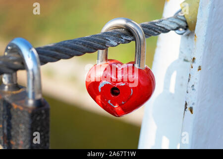 Red lock hang on a cable on a bridge. Symbol of eternal love and fidelity metal heart-shaped lock on the bridge close-up. Wedding traditions. Stock Photo