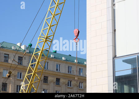 Close-up crane hook. A crane with a red hook on the background of multi-storey residential buildings. Building robots in the city. Stock Photo