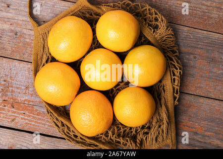 Top view of fresh organic oranges in string bag over old wooden rustic background. Close up Stock Photo