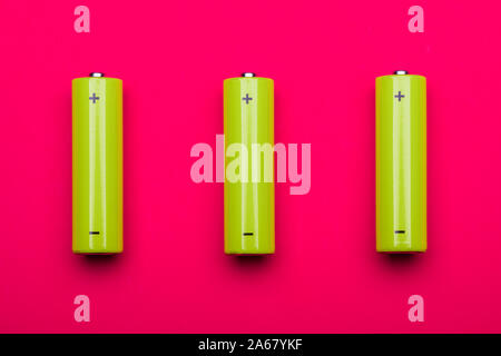 Top view of 3 yellow green AA alkaline or rechargeable NiMH batteries on pink background Stock Photo