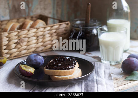 Bread toast with plum jam, served with milk and plums on a wooden background. Rustic style. Stock Photo