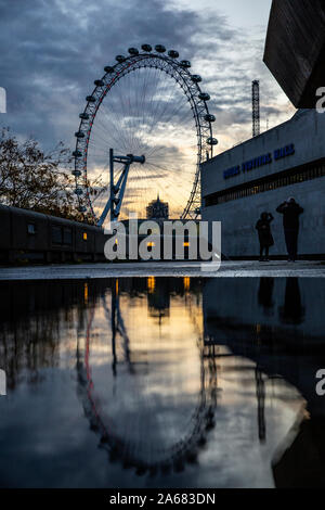 London Eye reflected in a puddle next to the Royal Festival Hal on a wet Autumn evening, Southbank, London, England, UK Stock Photo