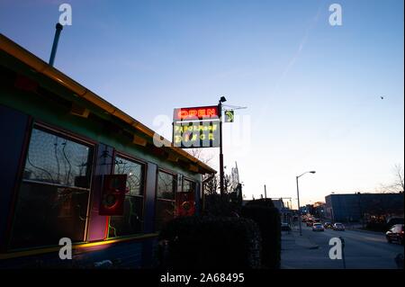 Low-angle evening shot of cars driving on a road next to a building with a neon sign advertising the Papermoon Diner, Baltimore, Maryland, January 8, 2008. From the Homewood Photography Collection. () Stock Photo