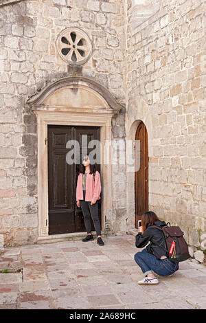 Two Asian girls take photos at the side door of  Saint Nicholas Serbian orthodox church in Kotor, Montenegro. Stock Photo