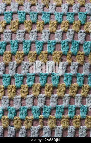 Old woolen knitted fabric in a mesh. Green, white, yellow threads. Deep hole texture. Knitted cover on a chair. Vertical. Stock Photo