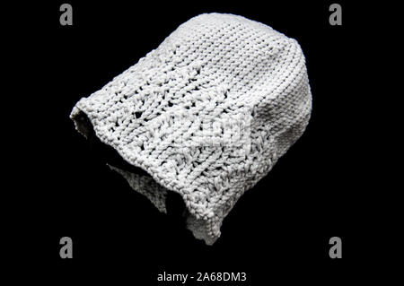 Light gray knitted hat fashion accessory for winter against a black background. Stock Photo