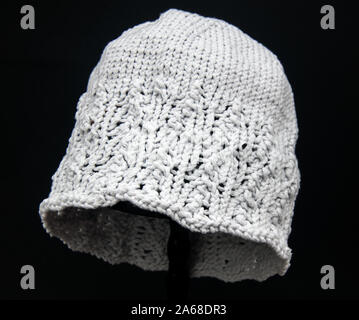 Pale gray knit hat fashion accessory for winter on a black background.  Fiber art clothing related craft object with detailed stitches, Stock Photo