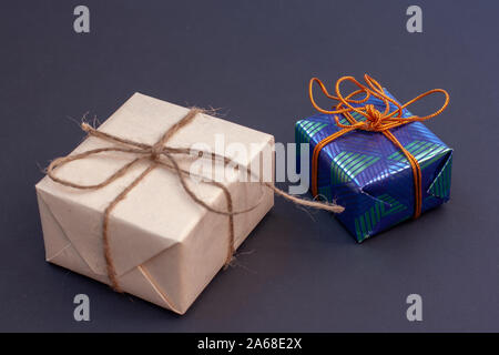 Two gift boxes on a dark background. One of the craft gray paper tied with a hemp rope, the second of glossy blue with green tied with an orange rope. Stock Photo