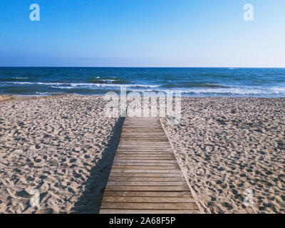 Wooden path to the water on a sandy beach by the sea under blue sky Stock Photo