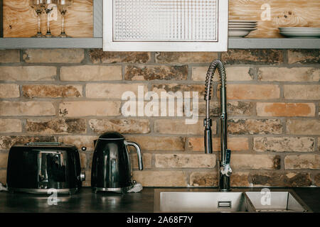 Kitchen with a brick wall with a faucet, kettle, toaster and shelves on which plates and glasses. Stock Photo