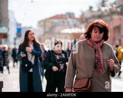 Moscow, Russia - October 19, 2019: A woman in coat and  scarf walks in a crowd of people dressed in demi-season clothes along the street. Warm autumn Stock Photo