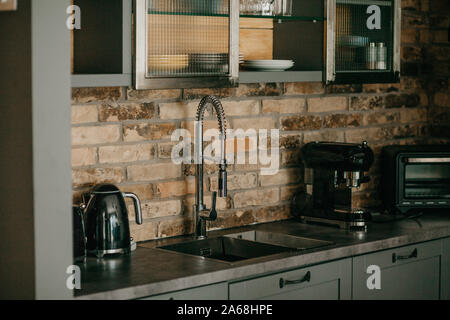 Kitchen with a brick wall with a faucet, kettle, coffee maker and shelves on which plates and glasses. Stock Photo