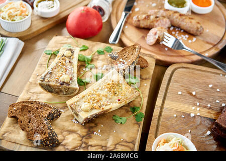 Beef bone marrow with chimichurri sauce and toasted bun. Barbecue restaurant menu. Many different food on the table. Dinner party or Banquet Stock Photo