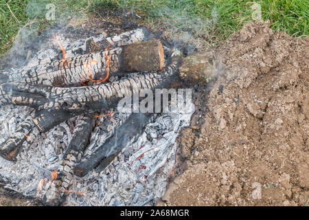 Outdoor camping survival wood fire in field. Shows fire pit with charred wood, embers and ashes. See explanatory notes for extra info. Stock Photo
