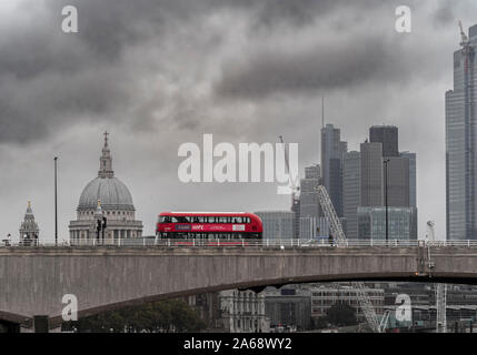 Waterloo Bridge over the river Thames on a grey misty day with a red double decker London bus passing over. St Pauls, and City of London office buildi
